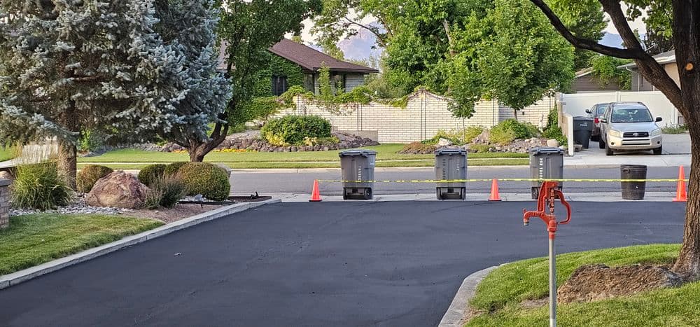 Street view showing garbage bins, traffic cones, and a parked vehicle near a residential area.