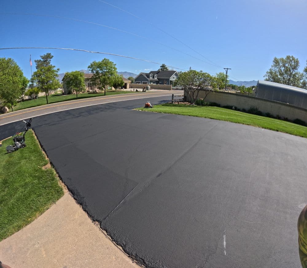Freshly sealed asphalt driveway with clear blue sky and suburban homes in the background.