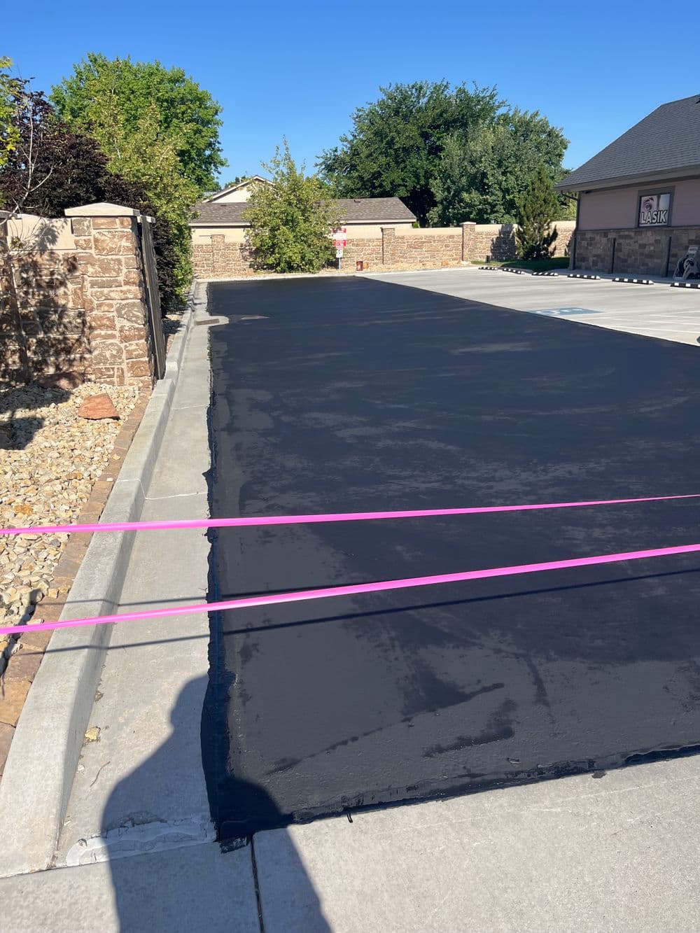 Freshly paved black asphalt driveway with pink construction markers and clear blue sky.