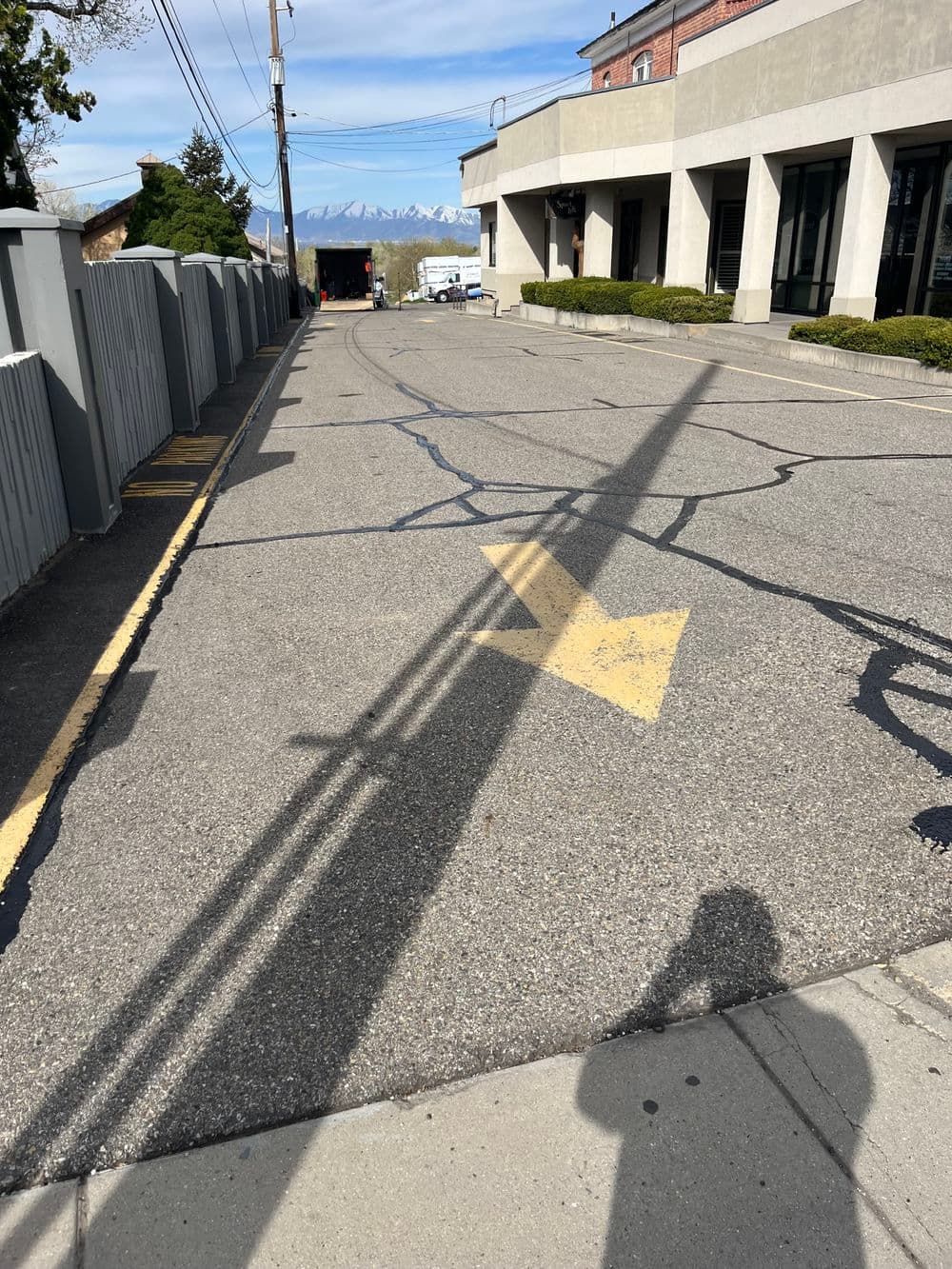 Empty street with cracked pavement and a yellow directional arrow, mountains in the background.