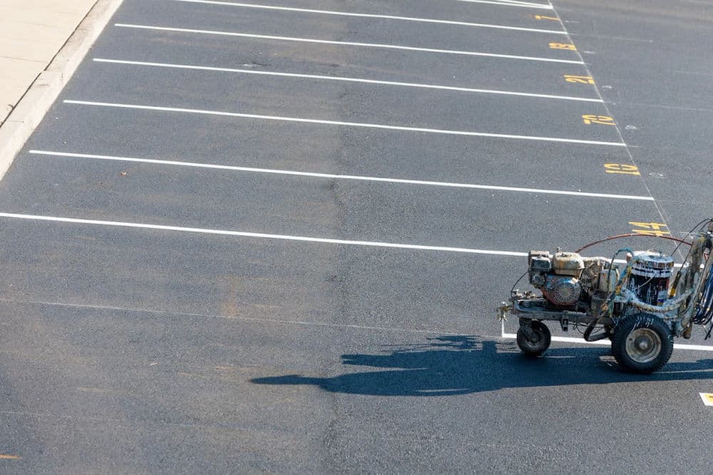 Parking lot striping machine painting lines on asphalt in an empty parking area.