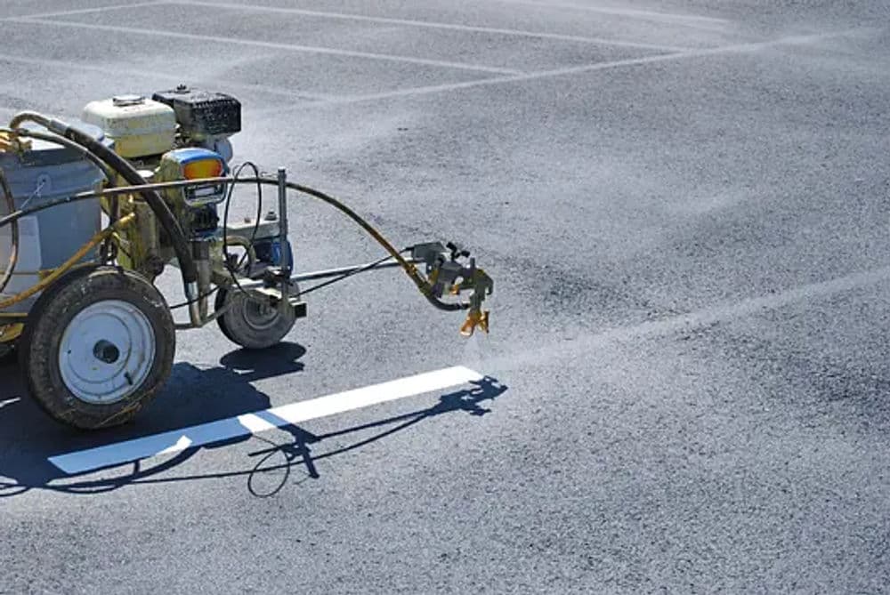 Line striping machine painting a white line on an asphalt parking lot.