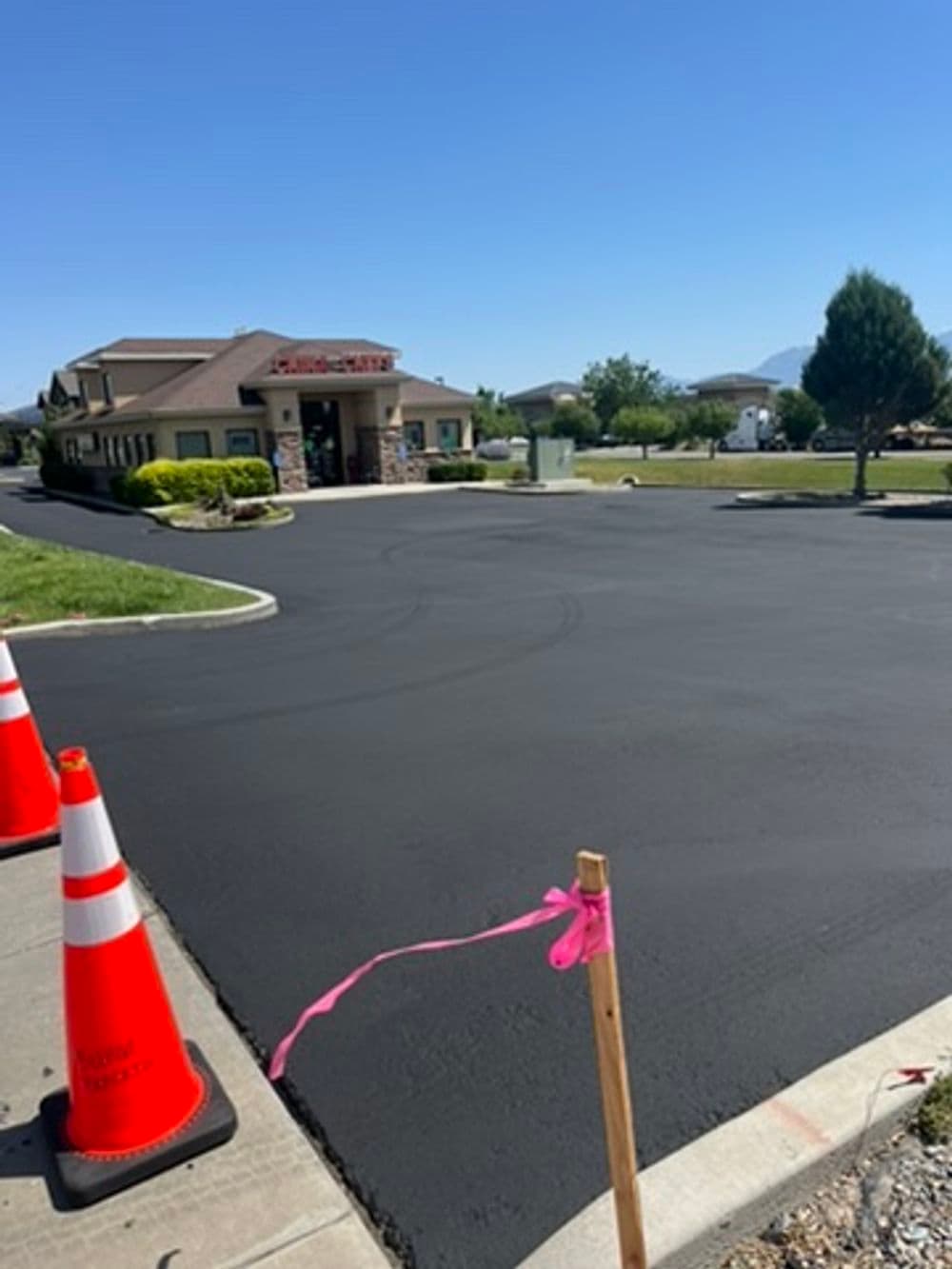 Freshly paved black asphalt parking lot with traffic cones and construction signage.