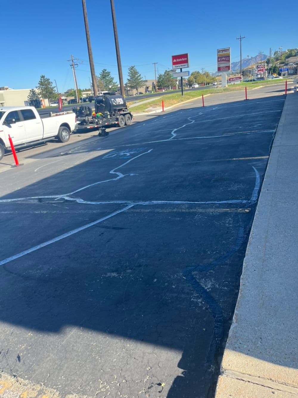 Parked truck with trailer in a commercial lot, showing cracked asphalt and red barriers.