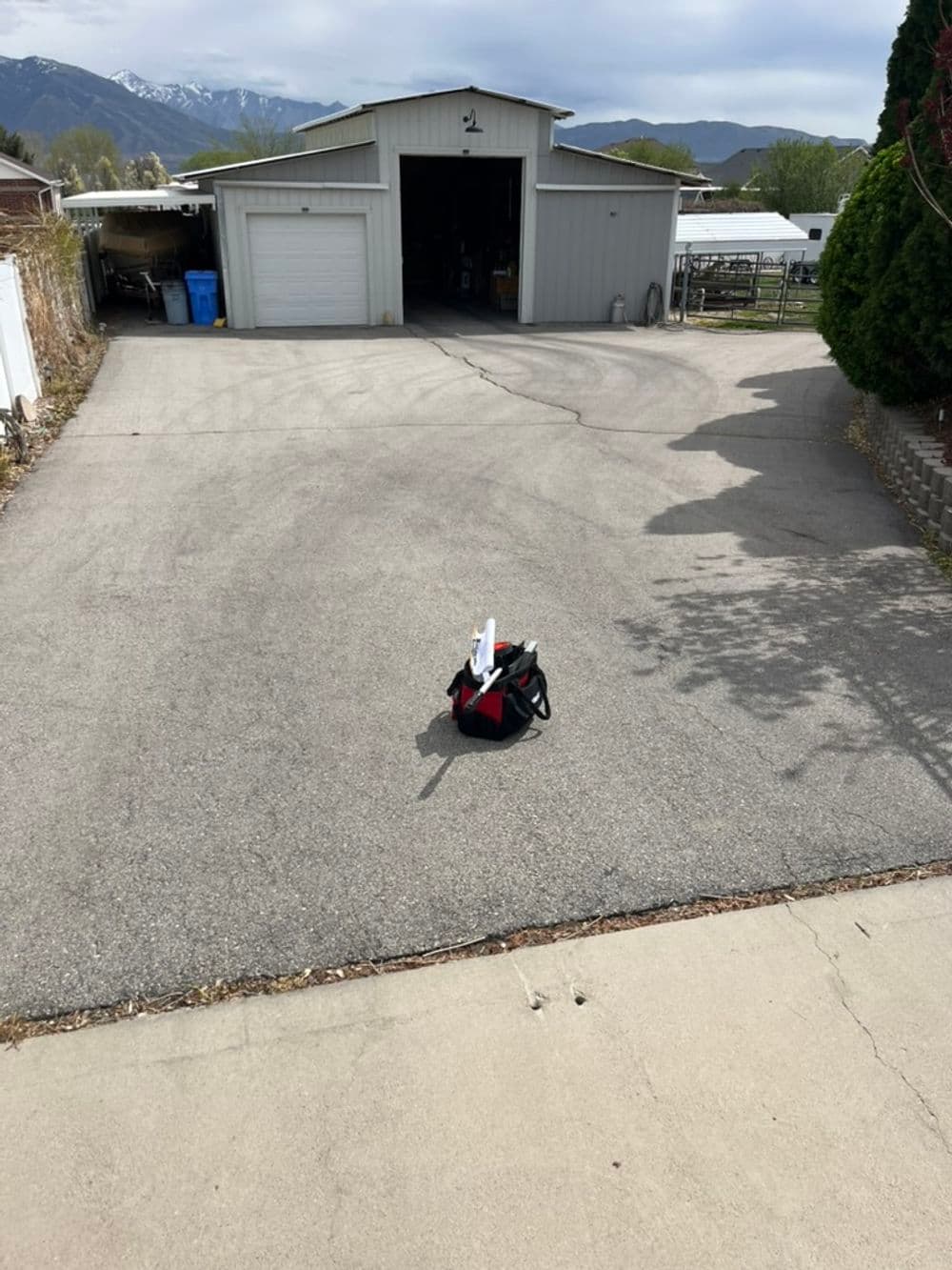 Red and black bag on a driveway near a garage and mountains in the background.