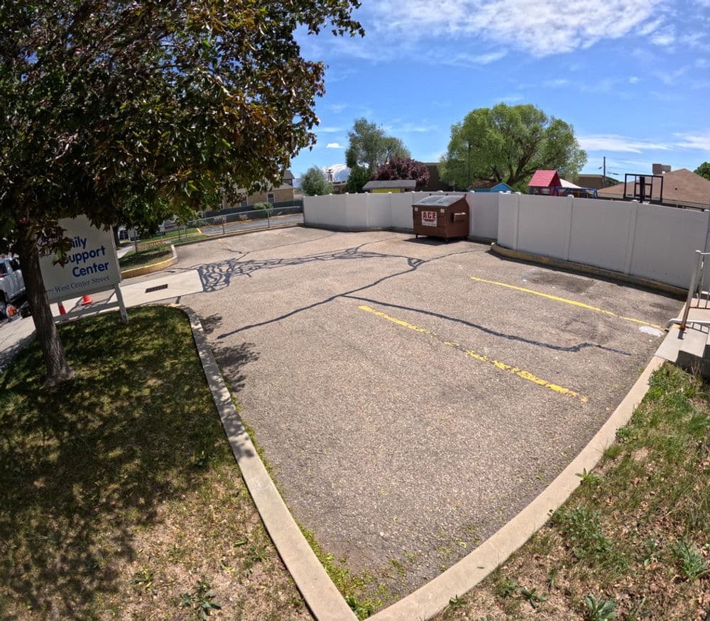 Empty parking lot near a support center with a dumpster and clear blue sky.