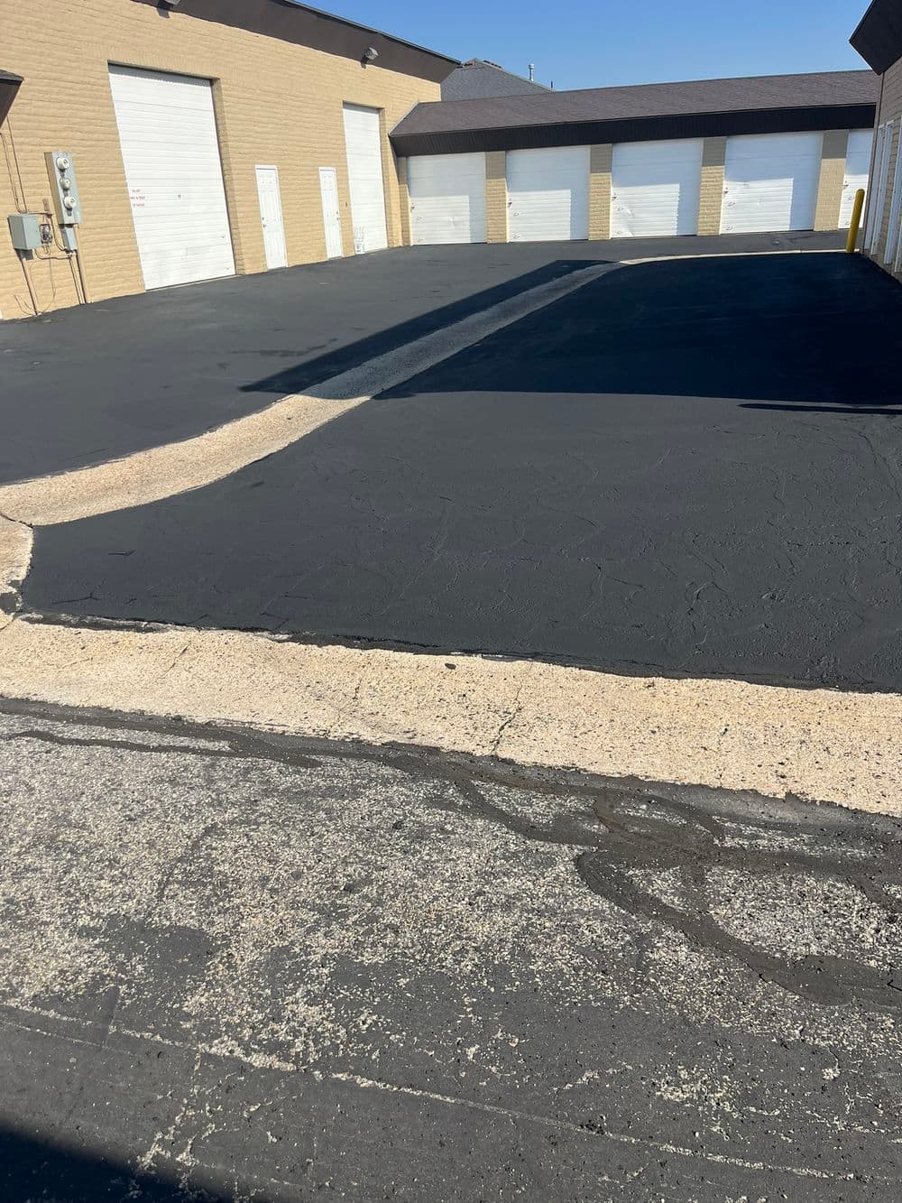 Freshly paved asphalt parking lot with storage unit doors in the background.