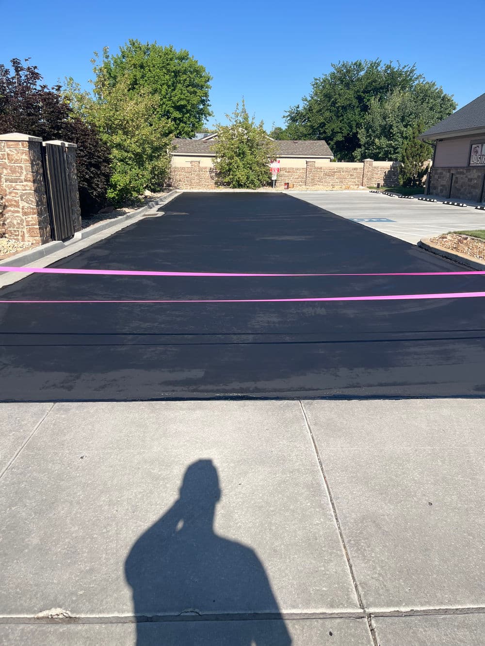 Freshly sealed black asphalt driveway with pink ribbons, clear blue sky in the background.