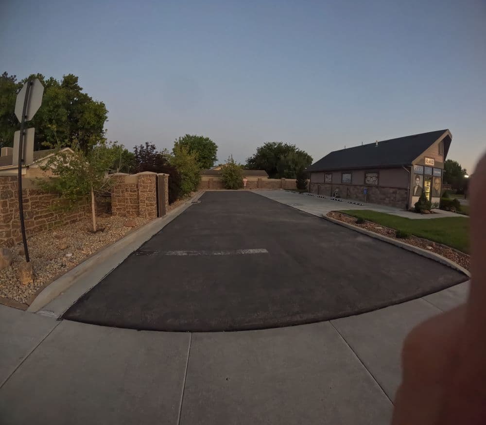 Empty asphalt driveway beside a stone wall and landscaped area at sunset.