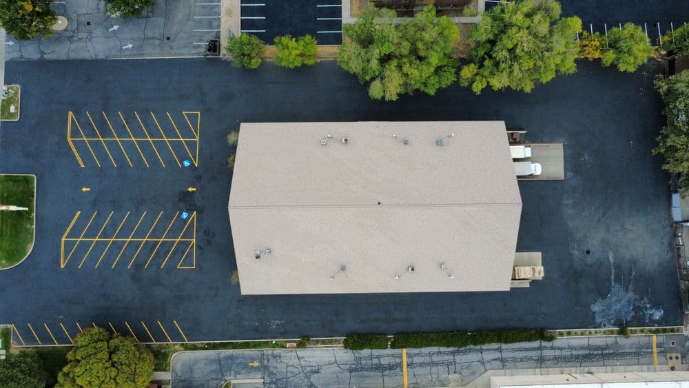 Aerial view of a parking lot with marked spaces and a tan building on a dark surface.