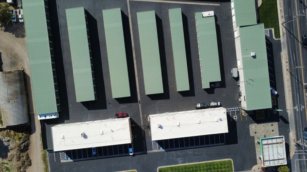 Aerial view of a storage facility with multiple green-roofed units and parking spaces.