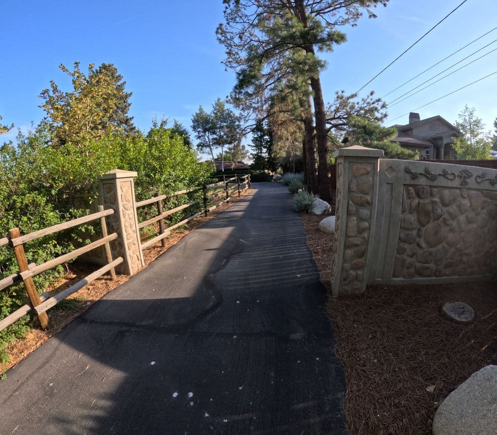 Paved driveway lined with trees and decorative stone walls leading to a house.